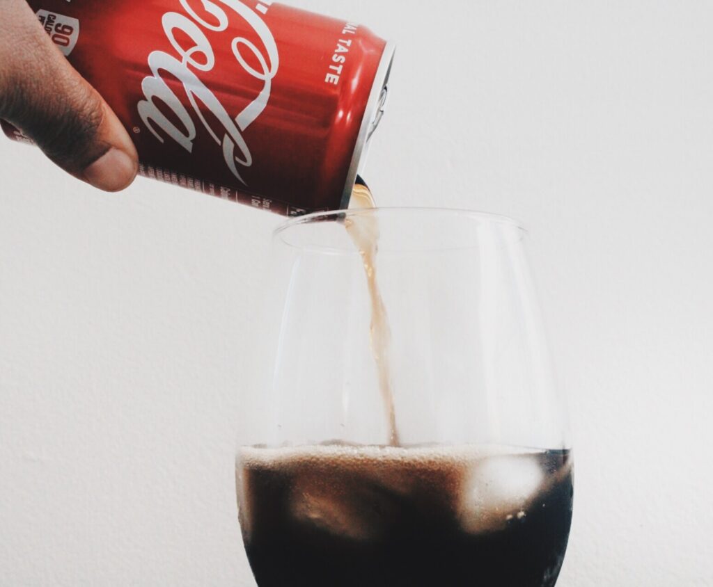 mano che versa CocaCola in un bicchiere