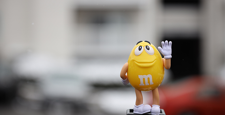 Mascotte M&M's gialla che saluta come esempio di un protagonista di un advergame illustrativo