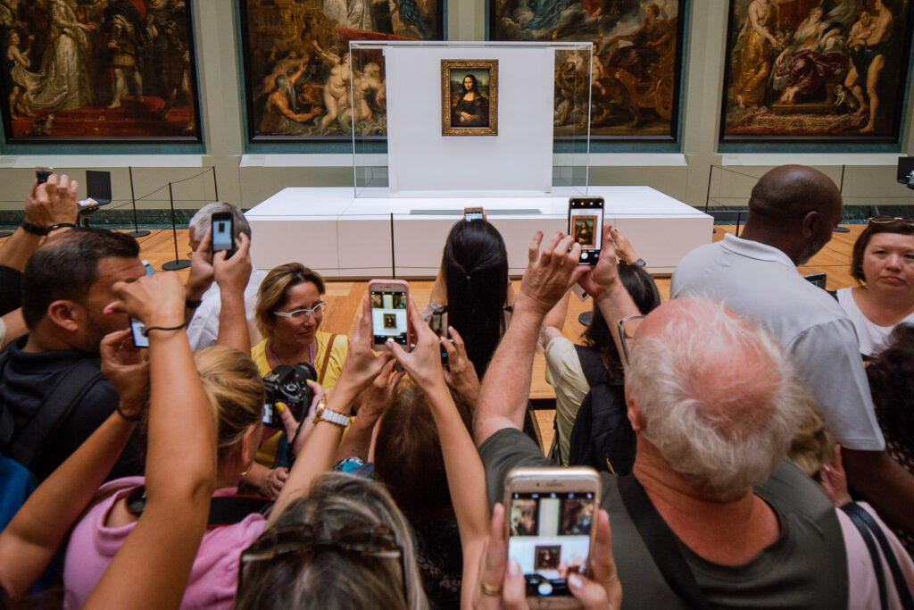 MONA LISA esposta a Museo Louvre, con persone che scattano foto con il telefono. 